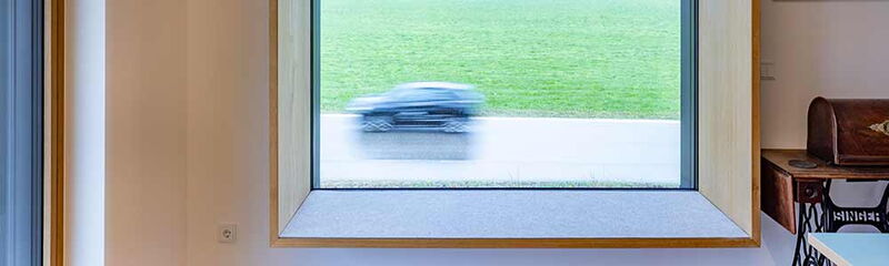 Blick durch ein Fenster auf eine Wiese, während ein Auto vorbeifährt. | © Name