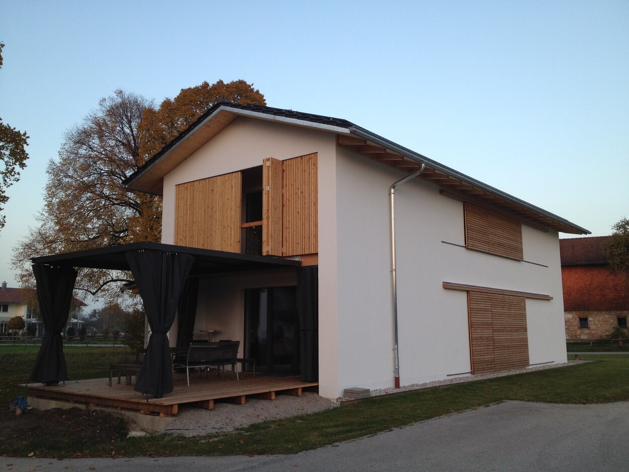 Ein modernes Passivhaus mit Holzverschalung und Terrasse steht malerisch in einer ländlichen Umgebung bei Übersee.
