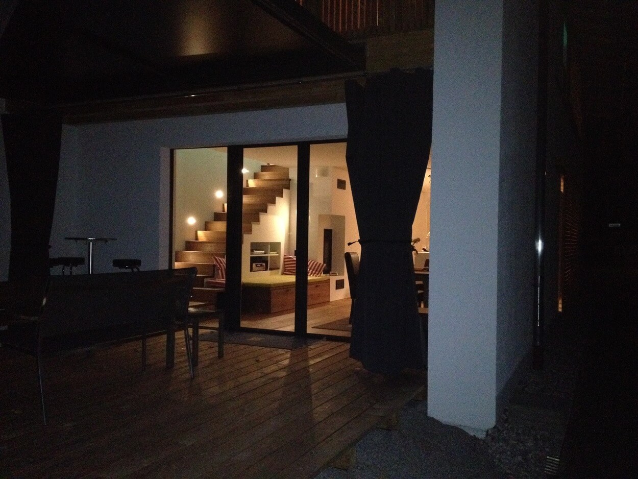 Ein Blick durch die Fenster eines Passivhauses zeigt ein stilvolles Wohnzimmer mit Treppe und moderner Beleuchtung.