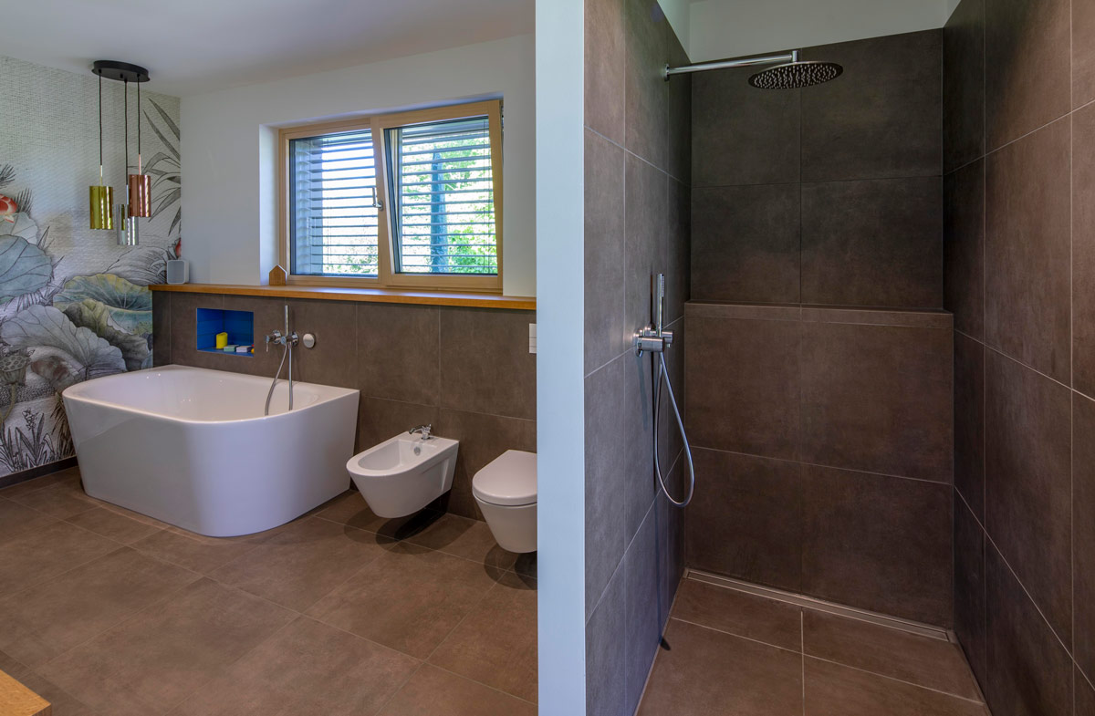 Ein modernes Badezimmer in einem Holzhaus in Glonn mit freistehender Badewanne, Duschkabine und kunstvoller Wandgestaltung.