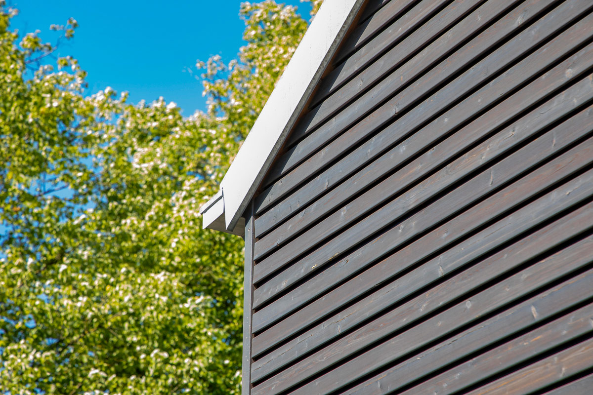 Die dunklen Holzlatten der Fassade eines Holzhauses in Glonn kontrastieren mit dem strahlend blauen Himmel.