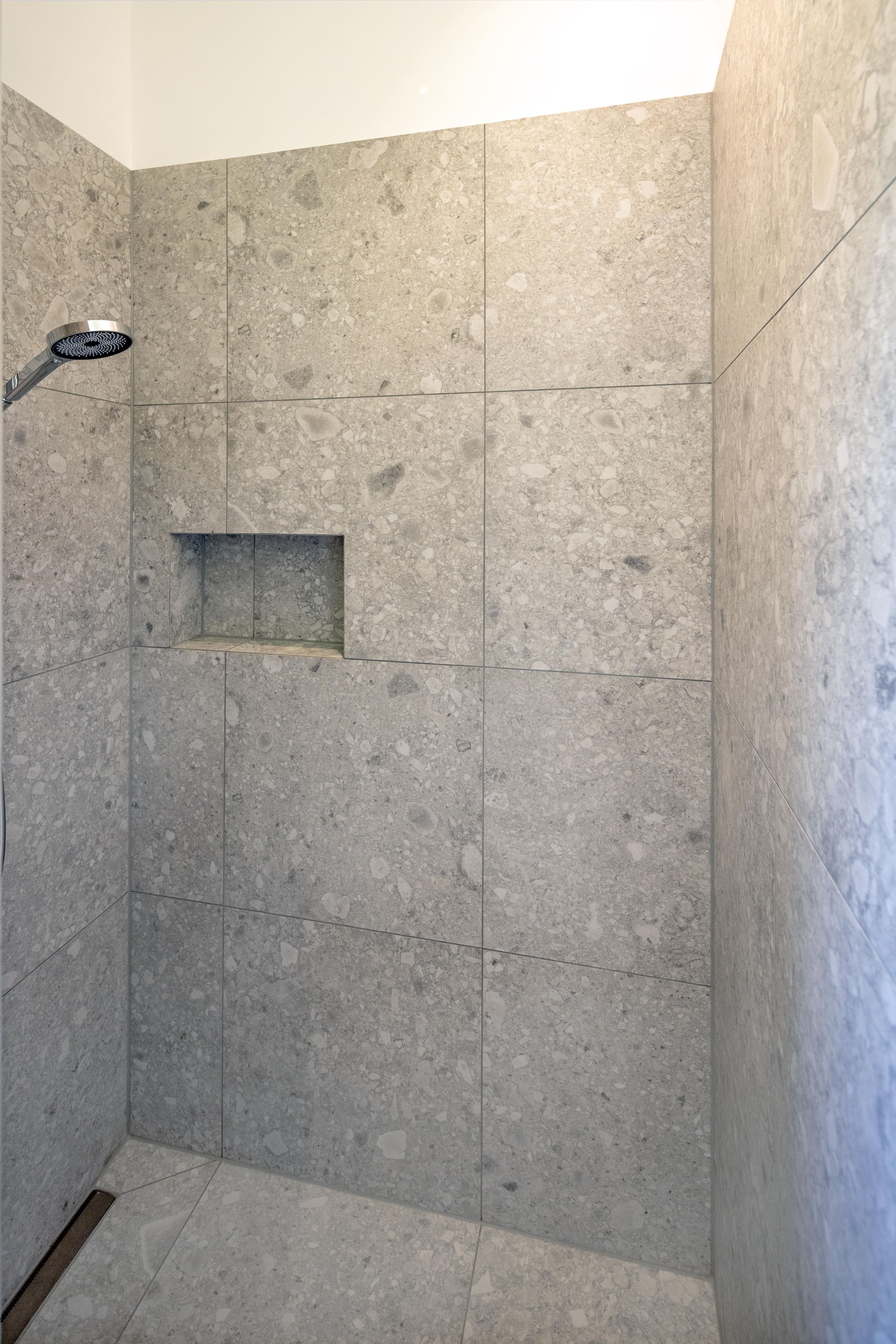 Eine moderne Dusche mit grauen Steinfliesen und einer eleganten Ablage verleiht dem Raum ein stilvolles Ambiente.