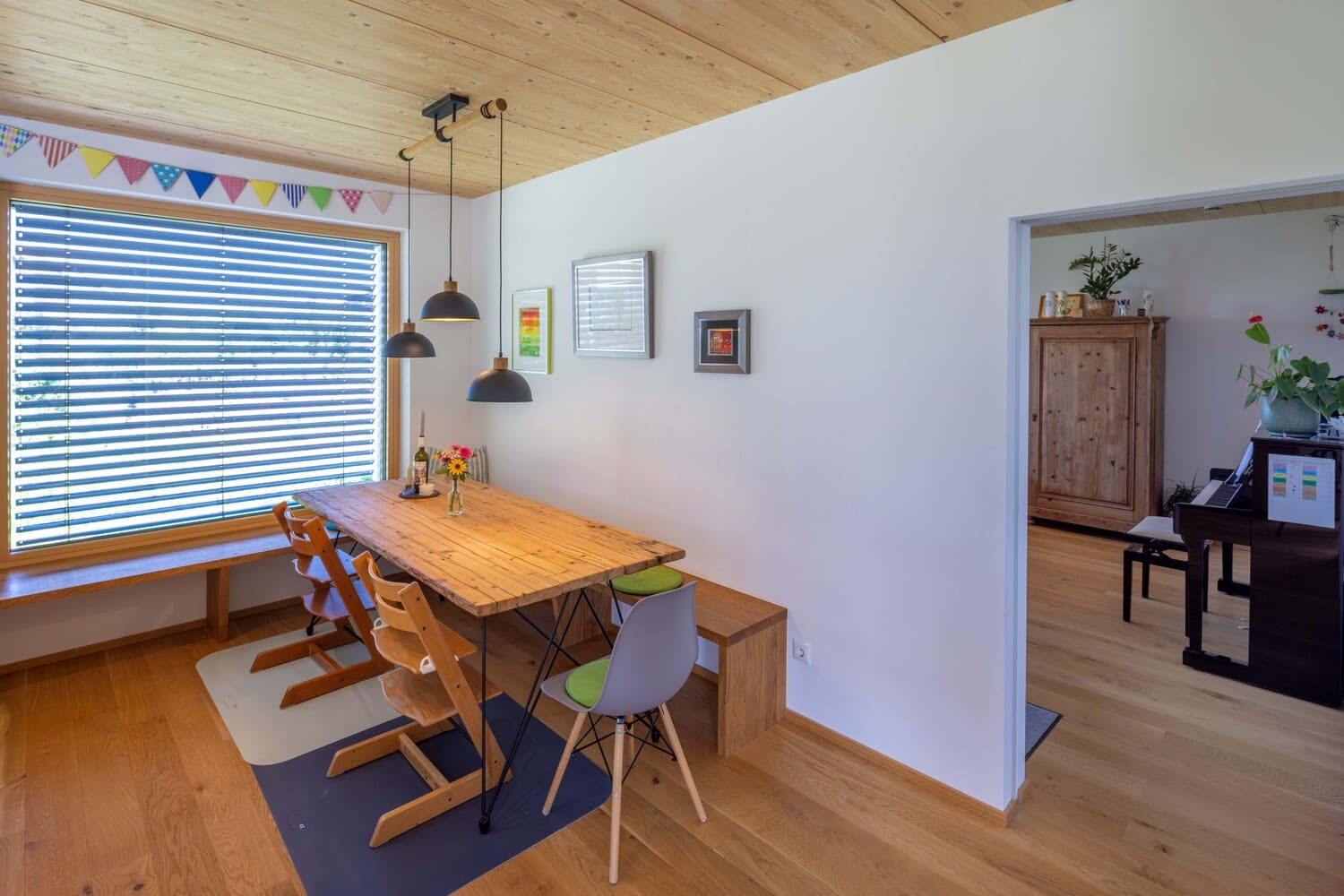 Ein Esszimmer mit Holztisch und bunten Stühlen führt zur Küche mit Holzschrank und Pflanzen, dekoriert mit modernen Lampen.