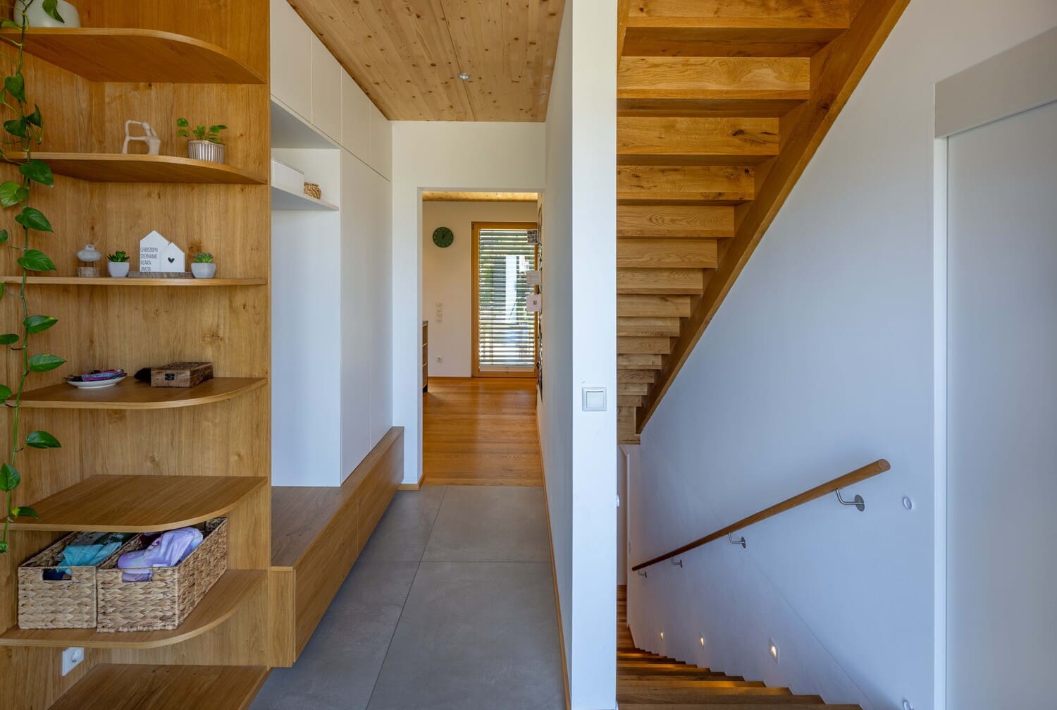 Ein modernes Interieur mit einem hölzernen Treppenaufgang, stilvollen Regalen und natürlichen Dekorationen prägt den Raum.